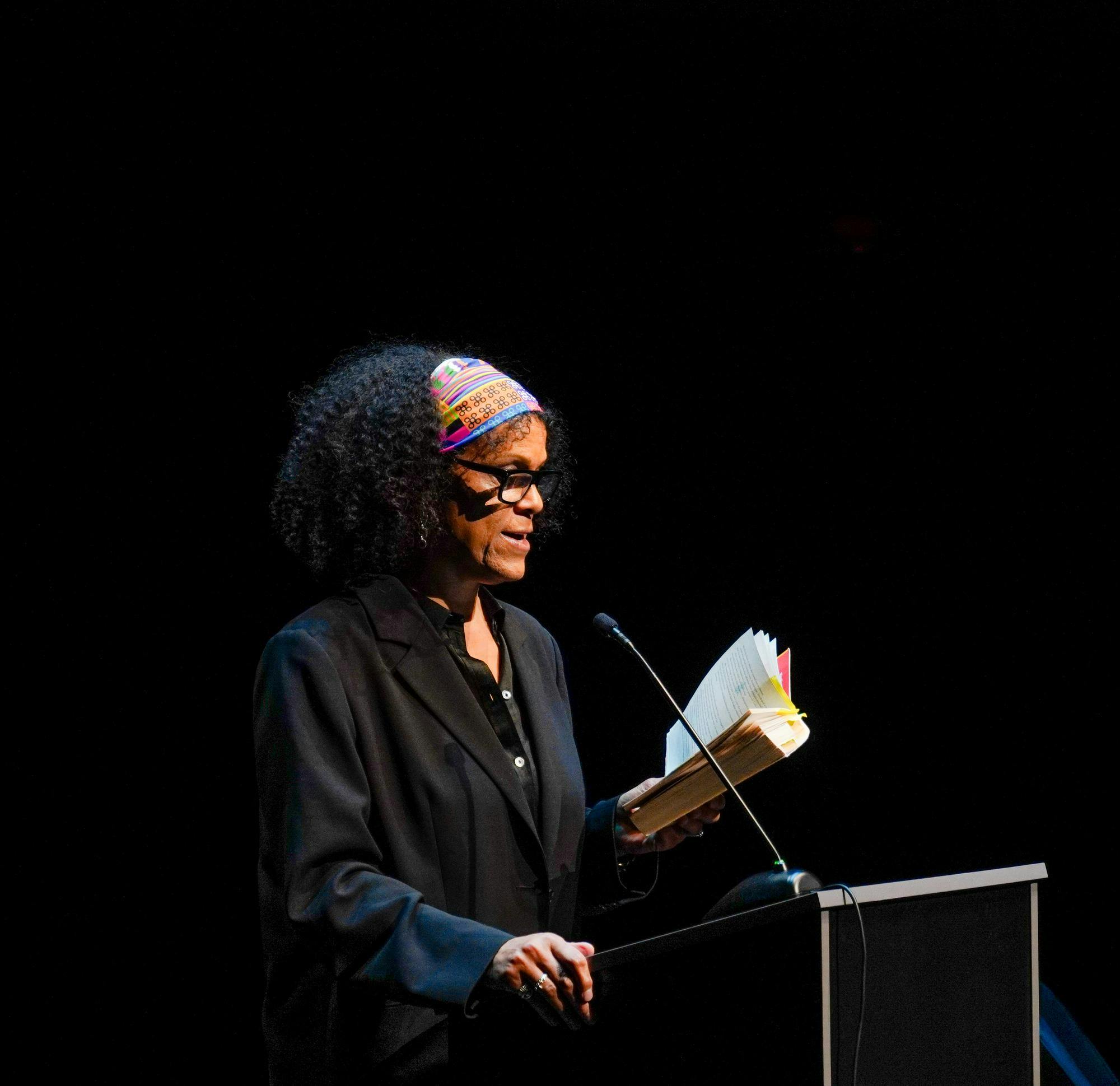 Bernadine Evaristo speaks into a mic on a podium, reading from her book.